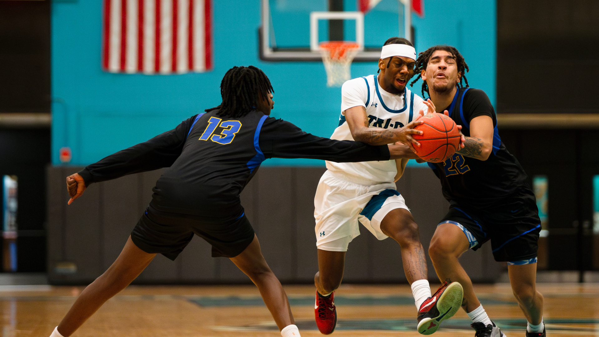 Tri-C basketball player Frankie Evans IV (in white) dribbles the basketball against two opposing players